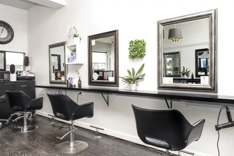 A photo of Vogue Hair & Barbers with three chairs facing the mirror and plants on the wall.